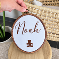 Cadre ovale avec prénom Noah et ourson brodés en marron sur fond blanc.
