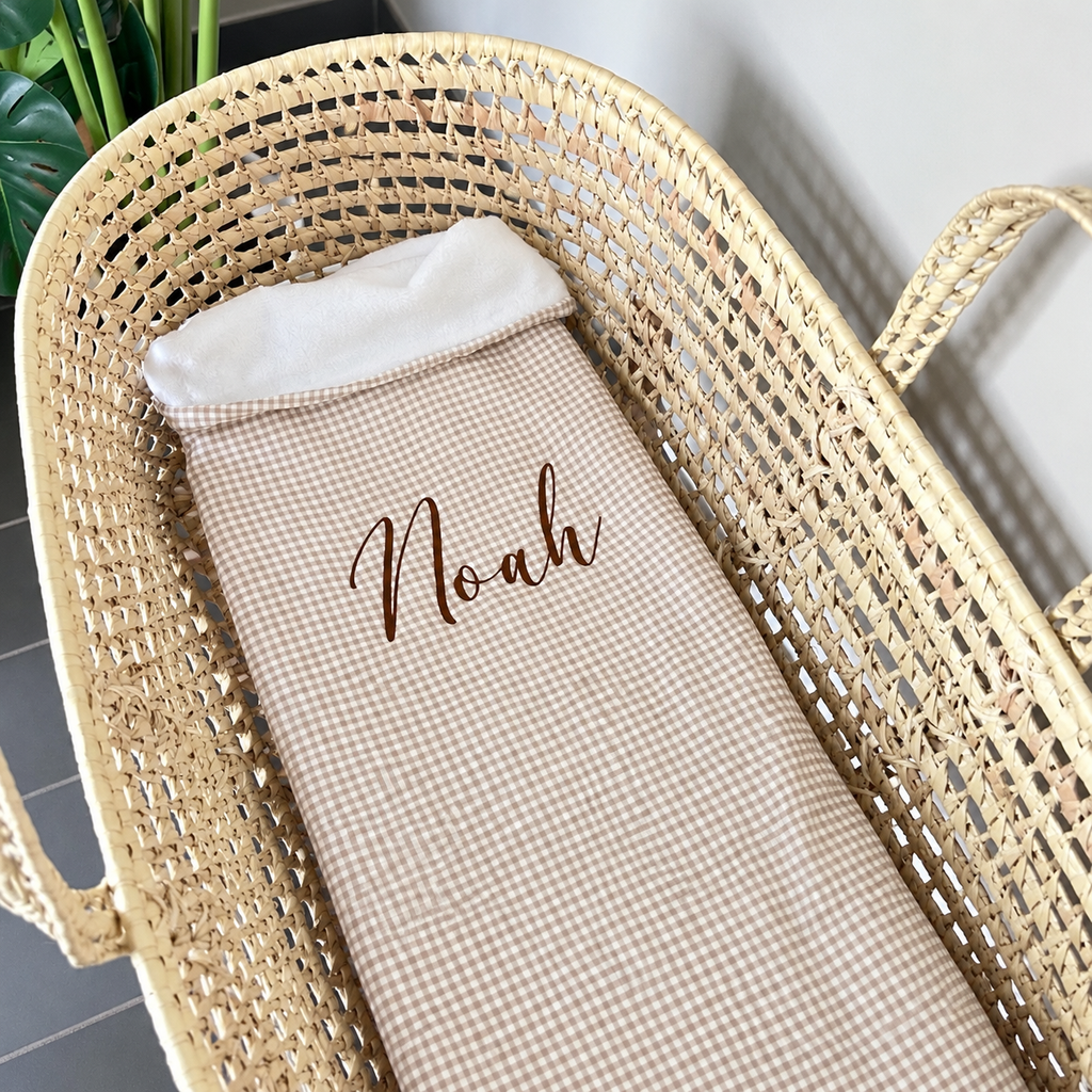 Couverture bébé Vichy beige brodée Noah dans un berceau, avec revers polaire blanc.
